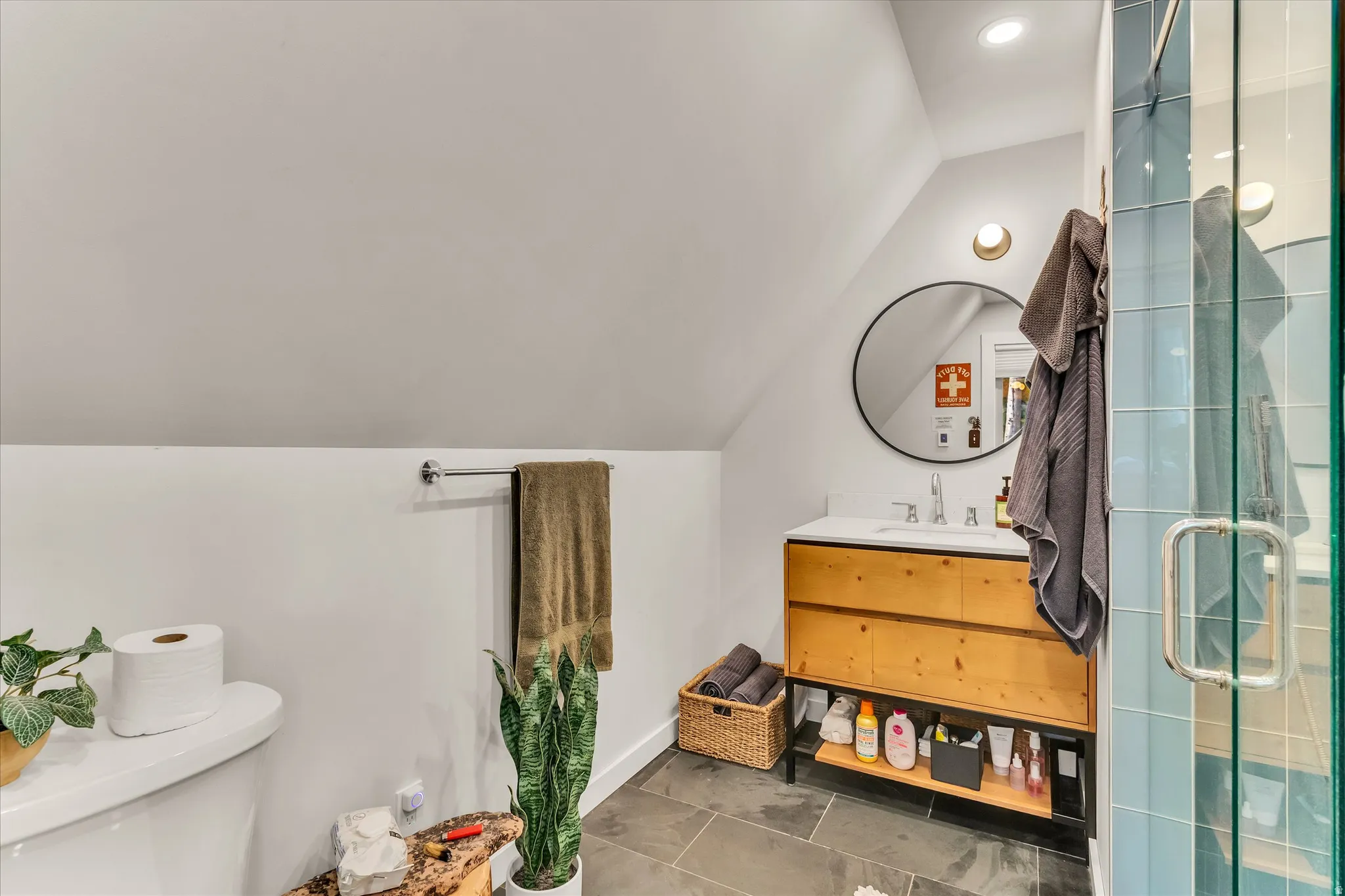 Contemporary bathroom featuring a light wood-finish vanity with integrated sink, circular mirror, and modern sconce lighting