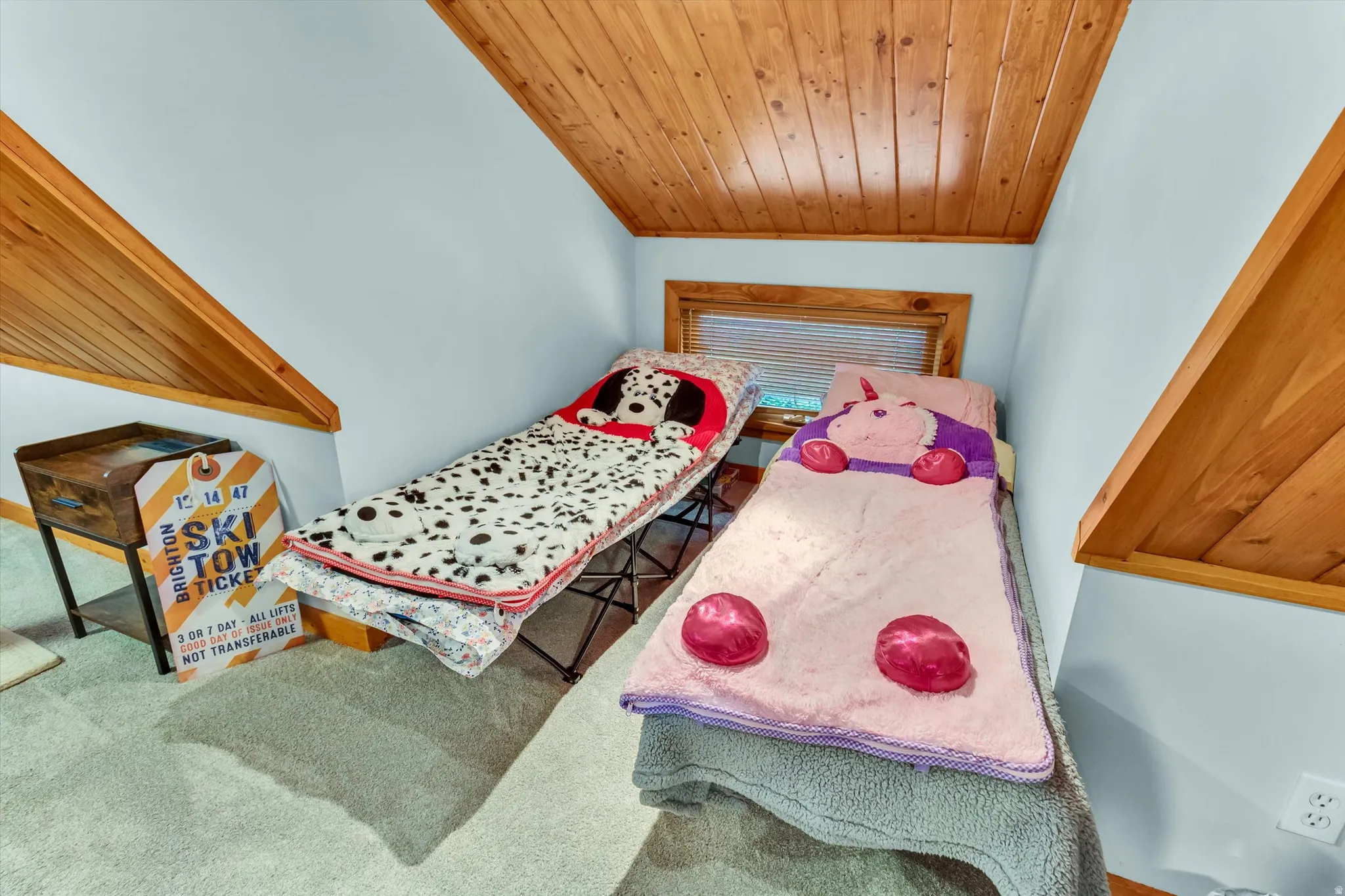 Attic space featuring pitched wood-paneled ceilings, light blue walls, and a wood-trimmed window