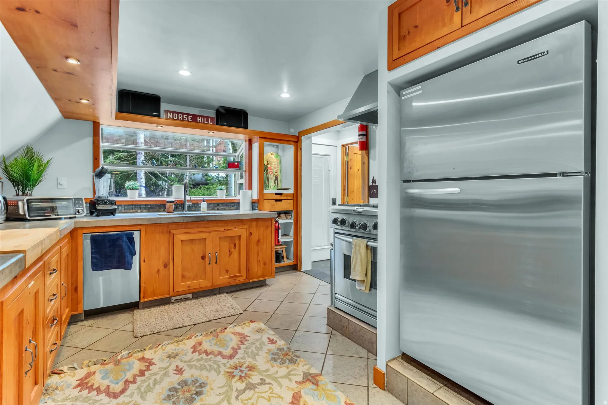 Kitchen featuring natural wood cabinetry, stainless steel appliances, tiled flooring, wood-finish countertops, and an integrated window over the sink