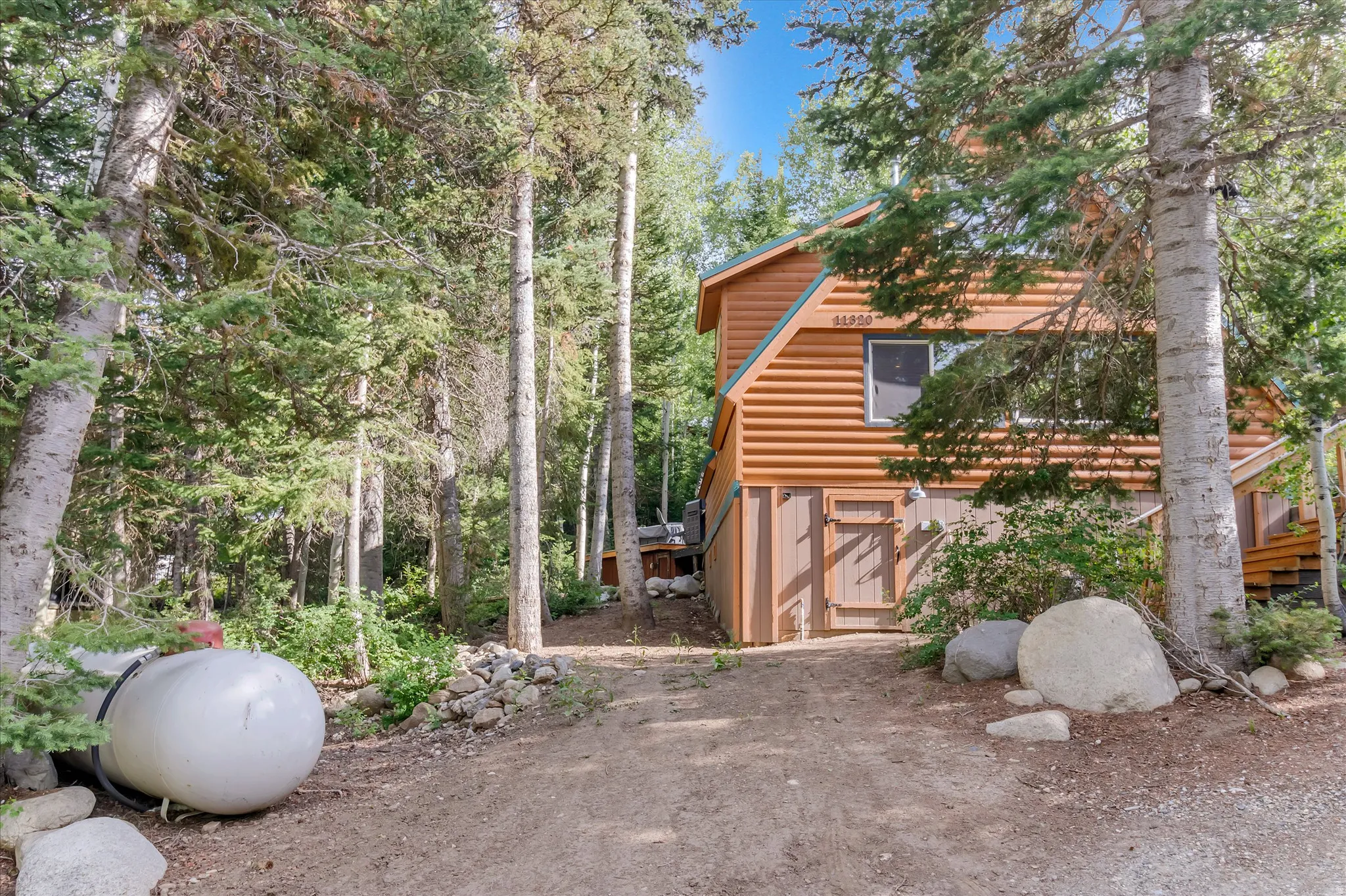 Wood-sided gable-roof home with exposed foundation and a natural stone-lined driveway