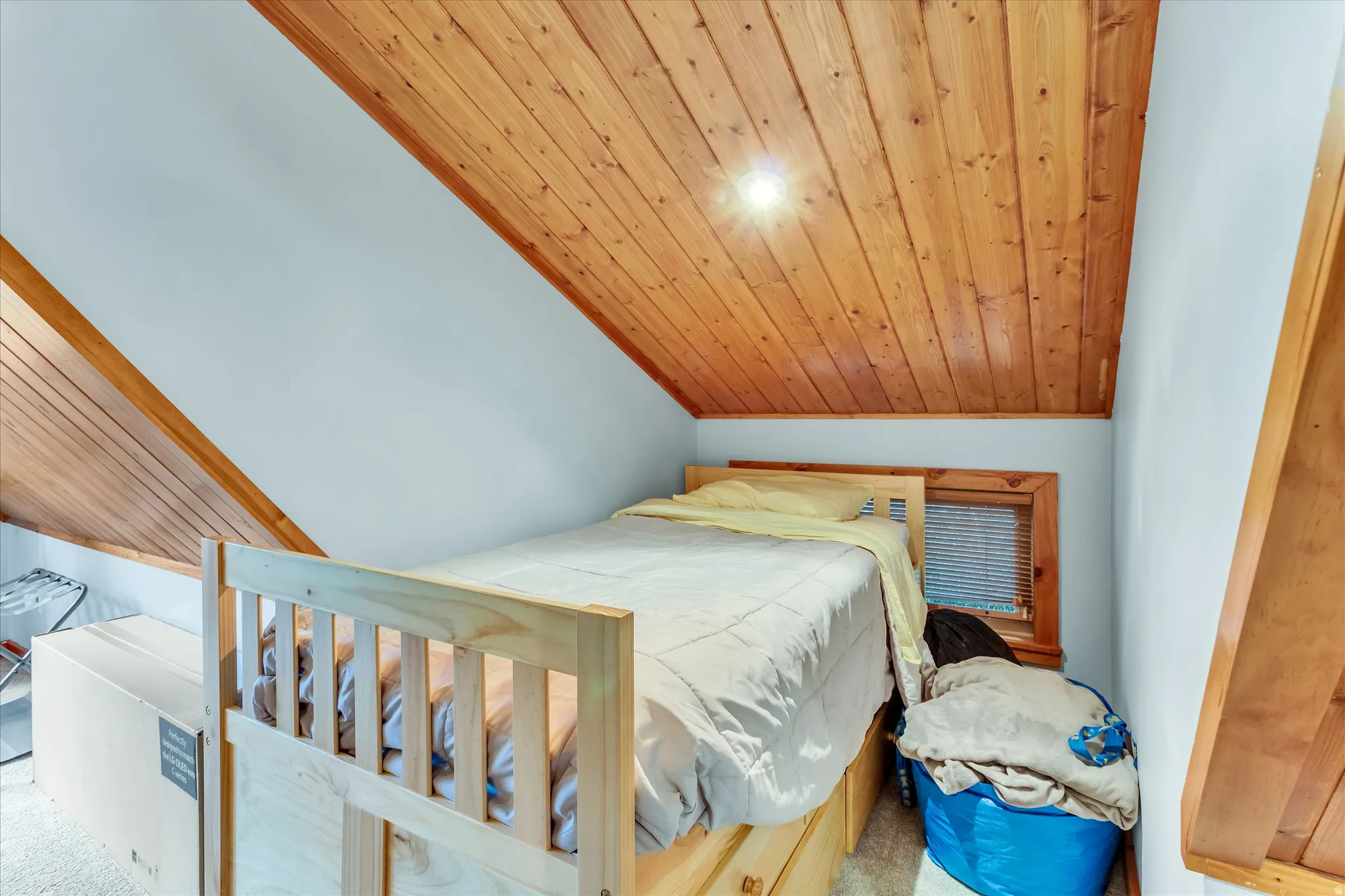 Attic room featuring a sloped wood-paneled ceiling, light-colored walls, and a window with wood trim