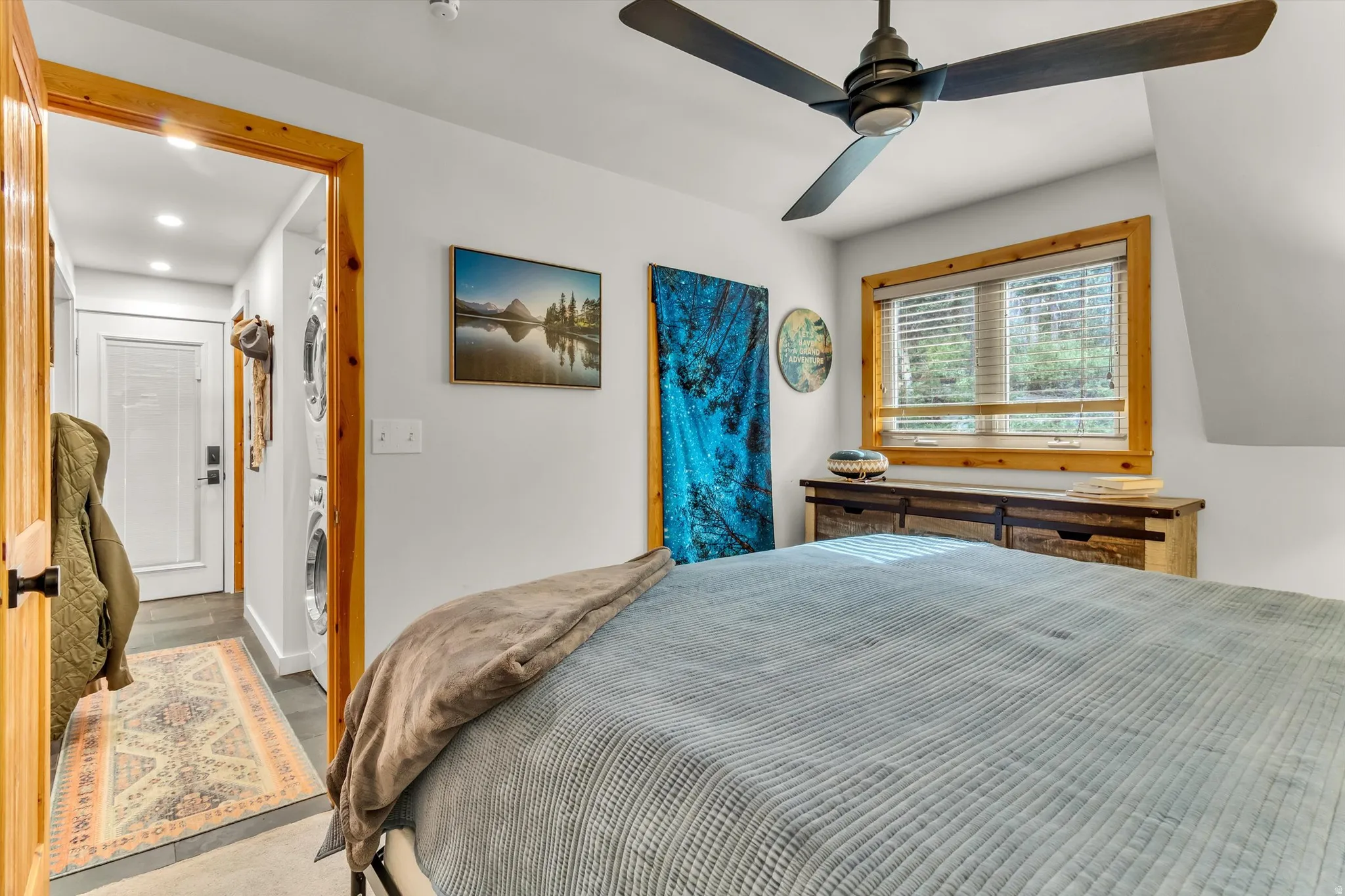 Bedroom featuring a ceiling fan with dark wood-finish blades, a wood-trimmed window with blinds, and light gray walls