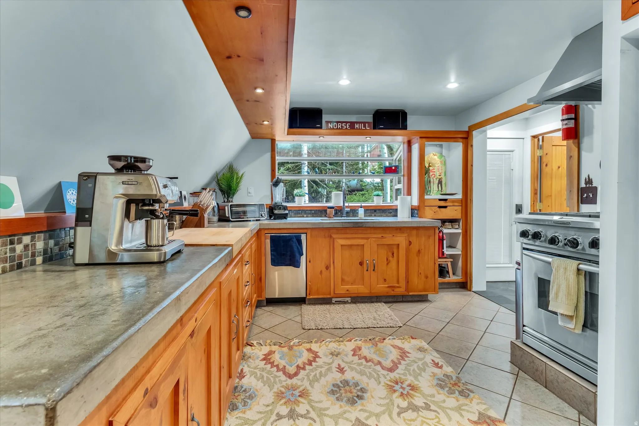 Kitchen featuring wood cabinetry, solid surface countertops, tile flooring, stainless steel range with hood, and built-in shelving