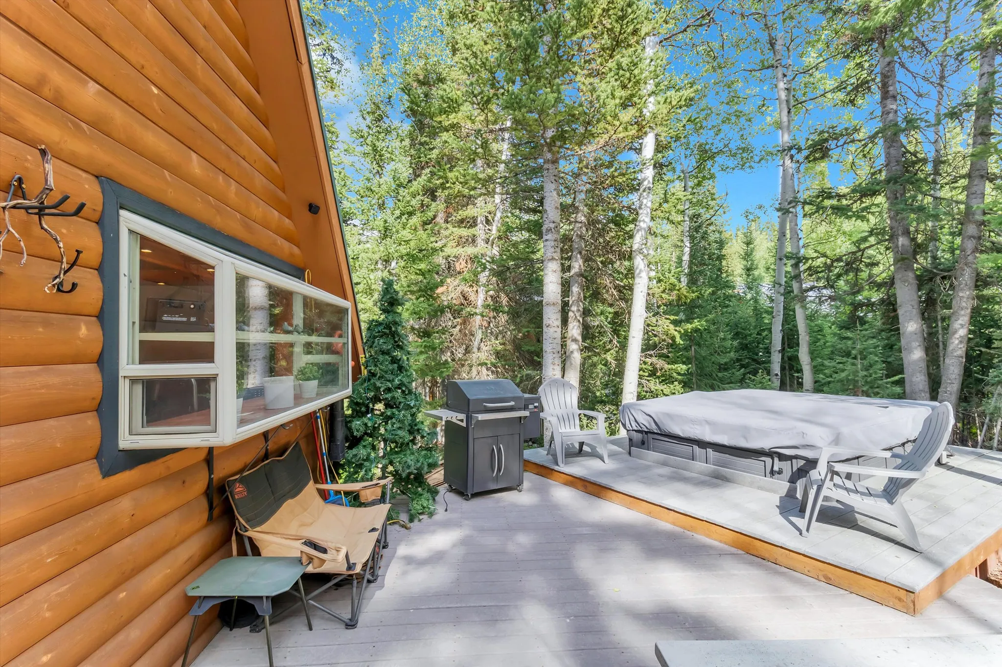 Wood-sided exterior featuring an elevated deck with a hot tub, surrounded by mature trees