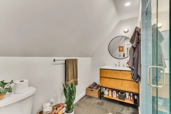 Contemporary bathroom featuring a light wood-finish vanity with integrated sink, circular mirror, and modern sconce lighting