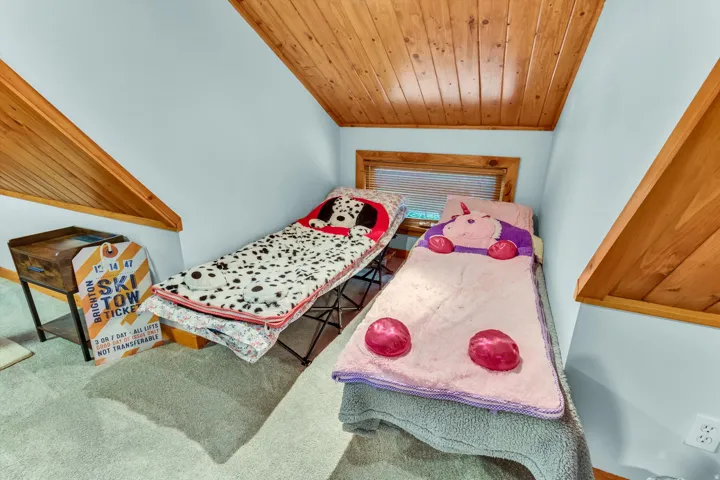 Attic space featuring pitched wood-paneled ceilings, light blue walls, and a wood-trimmed window
