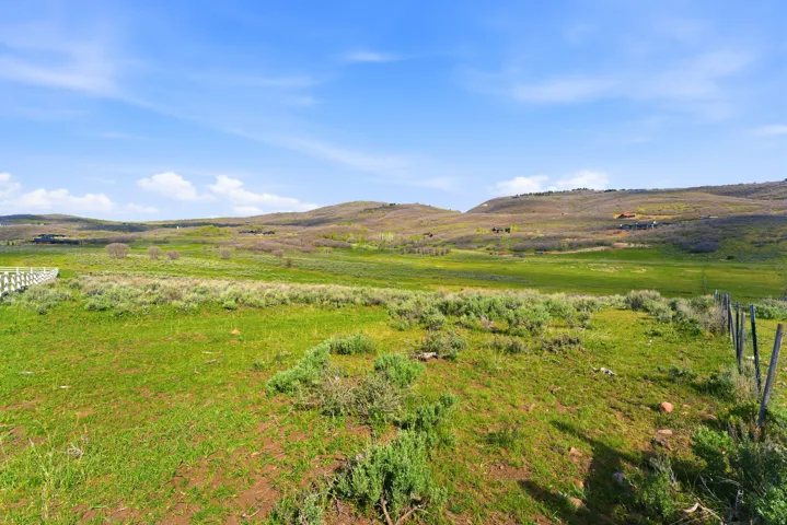 Expansive green landscape featuring rolling hills, scattered low-lying shrubs, and a partial white fence line