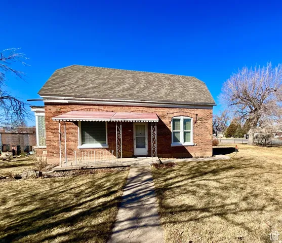 View of front facade featuring a shingled roof, brick siding, a front yard, and a porch