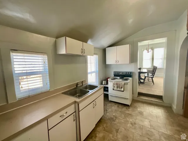 Kitchen with white electric stove, light countertops, vaulted ceiling, white cabinetry, and plenty of natural light
