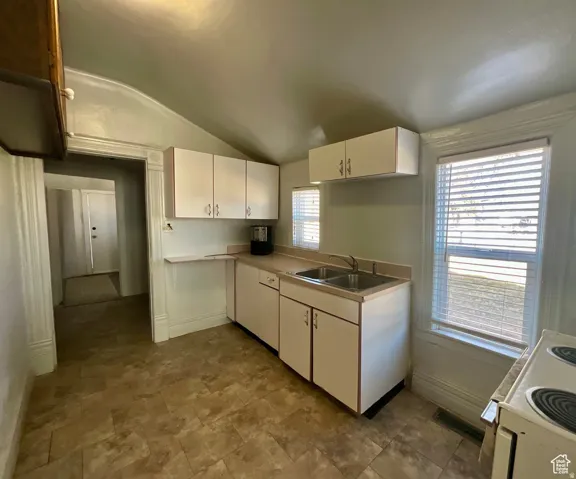 Kitchen featuring lofted ceiling, white cabinets, light countertops, electric range, and stone finish flooring