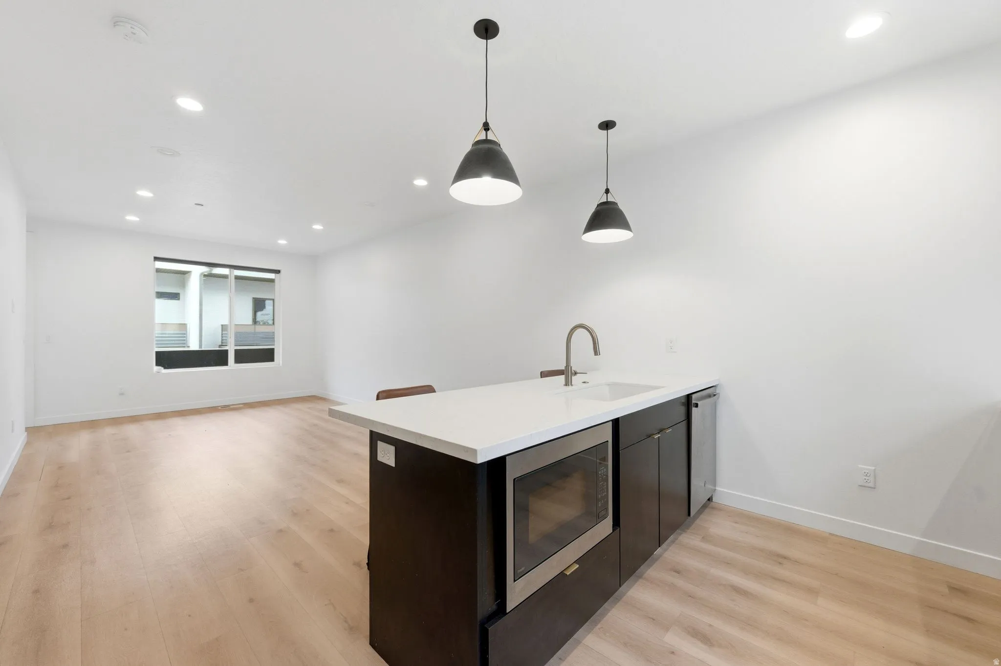 Kitchen with a peninsula, light wood-style floors, stainless steel appliances, hanging light fixtures, and light stone countertops