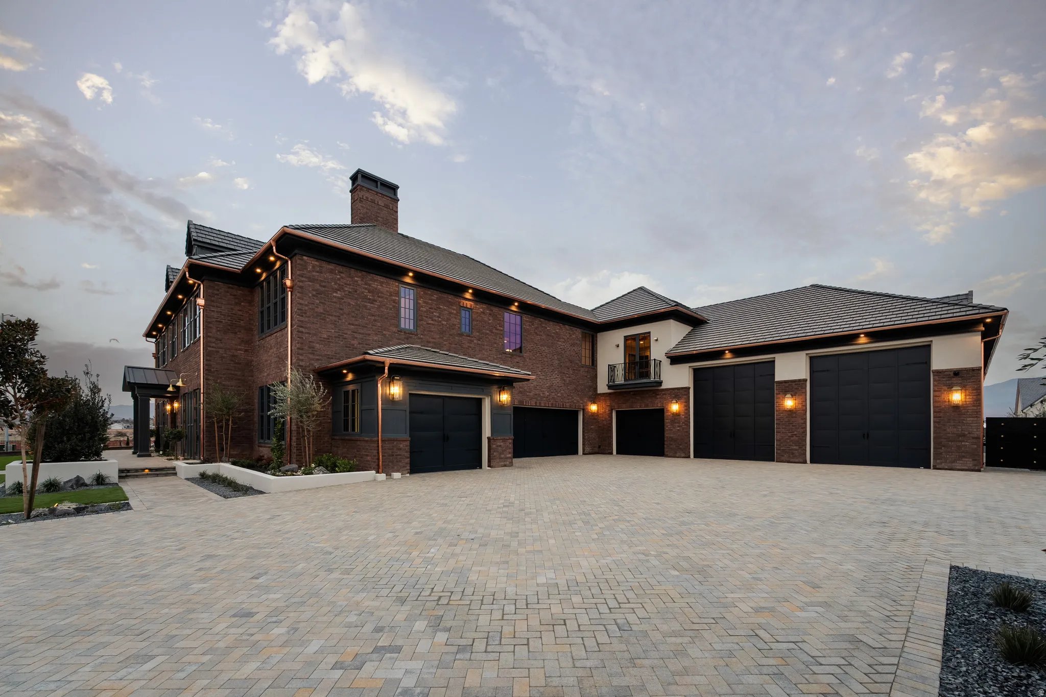 View of front of house featuring decorative driveway, a chimney, brick siding, and a balcony