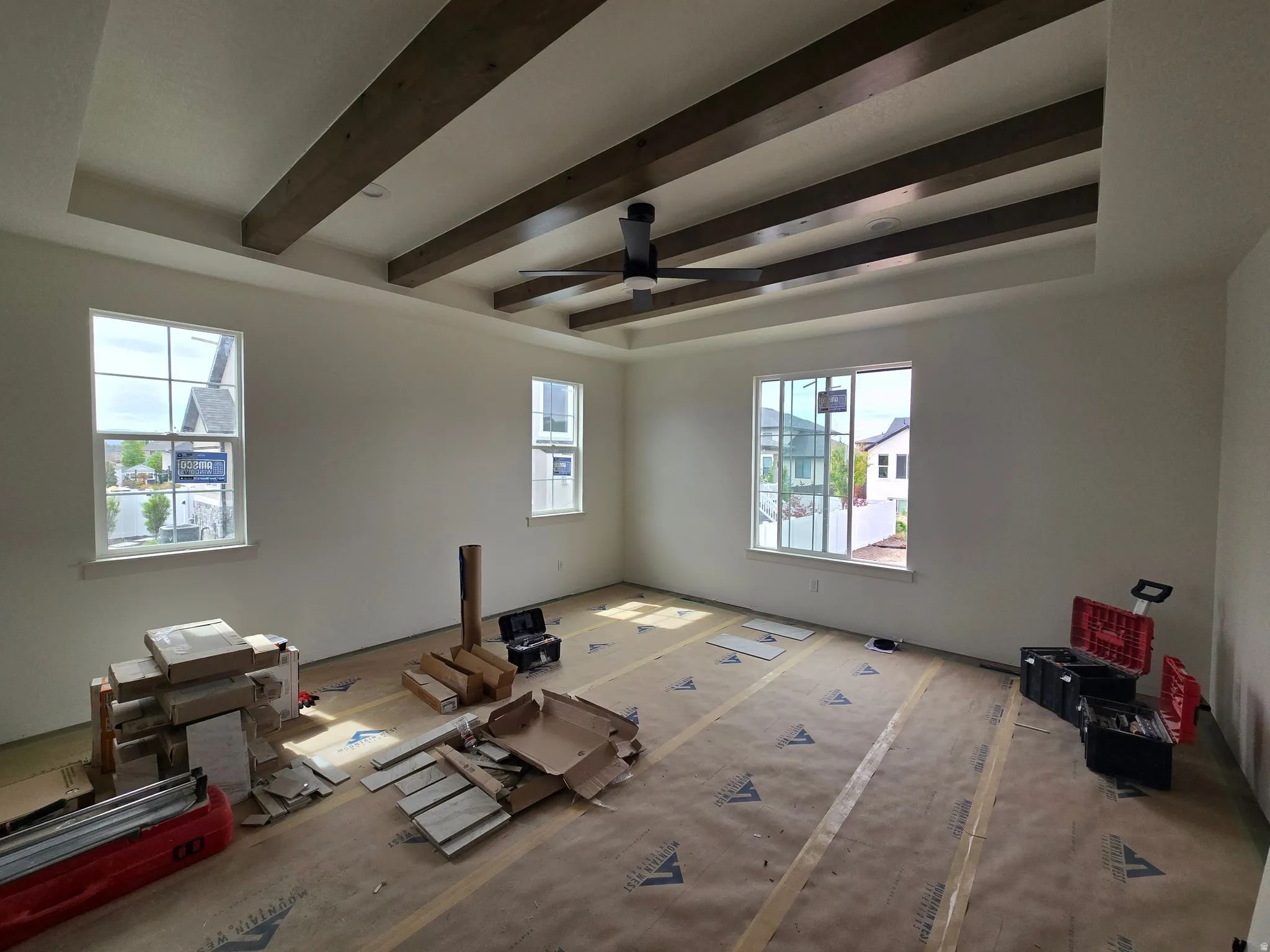 Unfurnished living room with ceiling fan, a tray ceiling, and beam ceiling