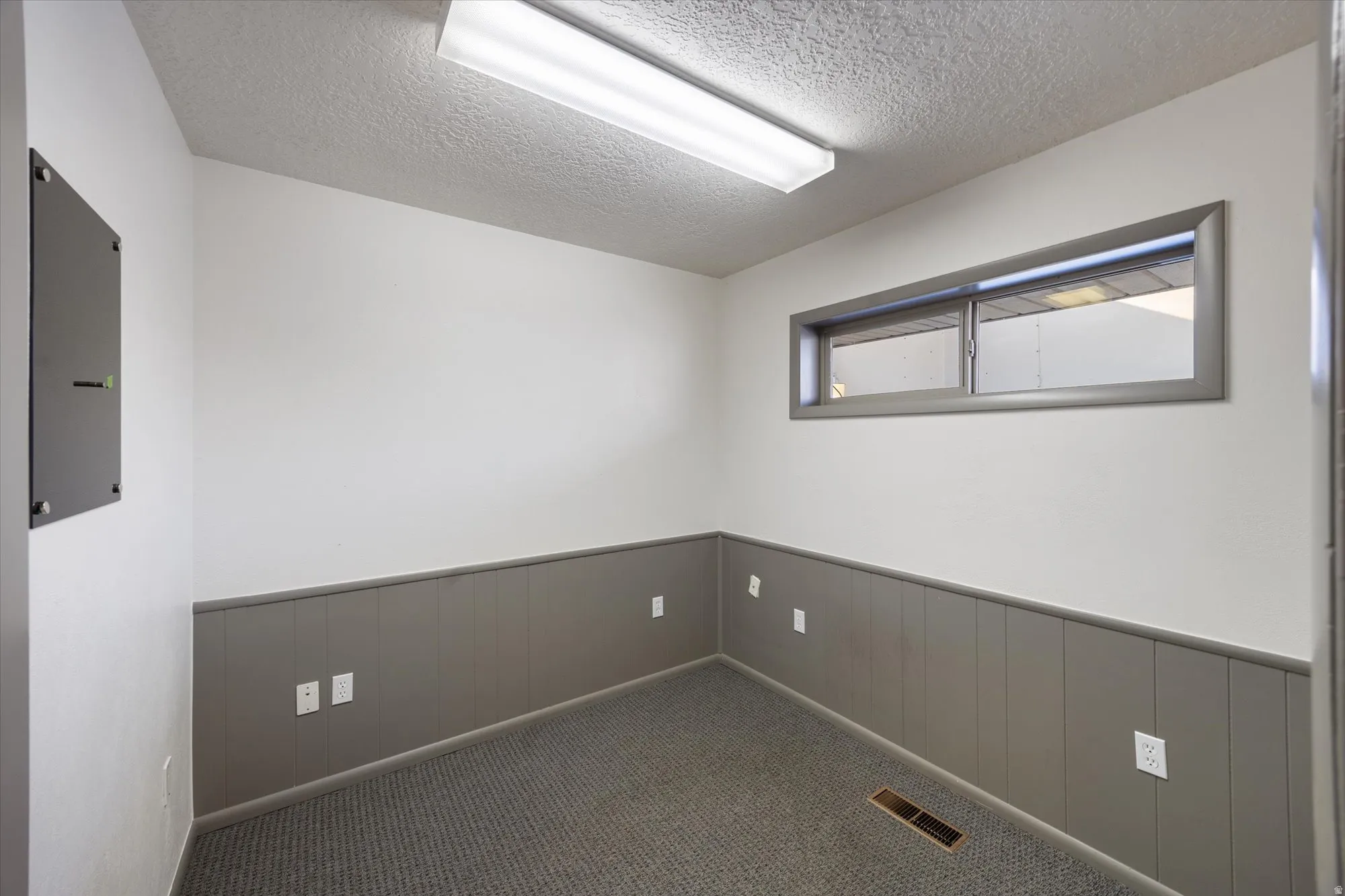 Carpeted spare room with wainscoting, a textured ceiling, electric panel, and wood walls