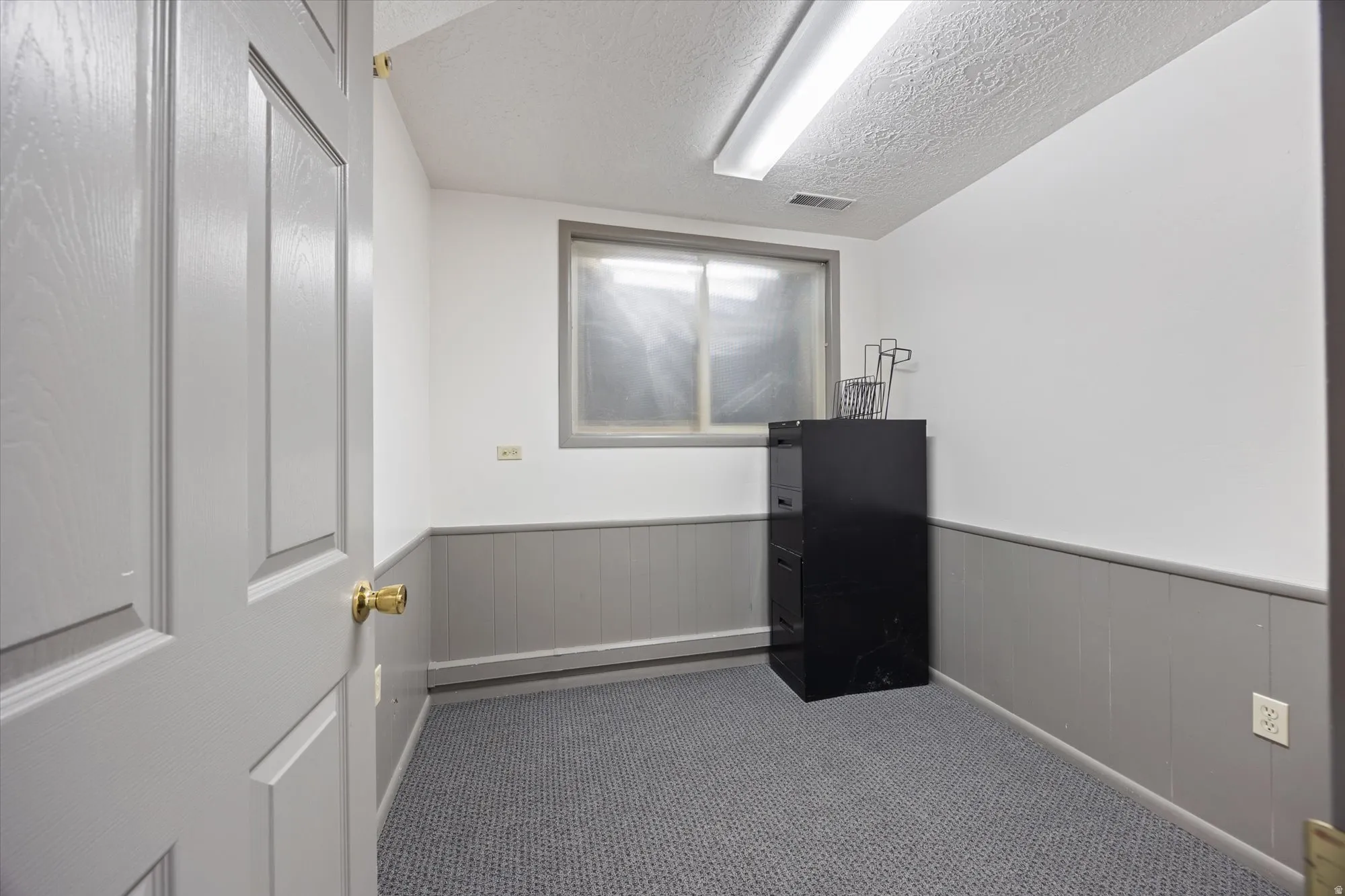 Unfurnished room featuring a wainscoted wall, a textured ceiling, and dark colored carpet