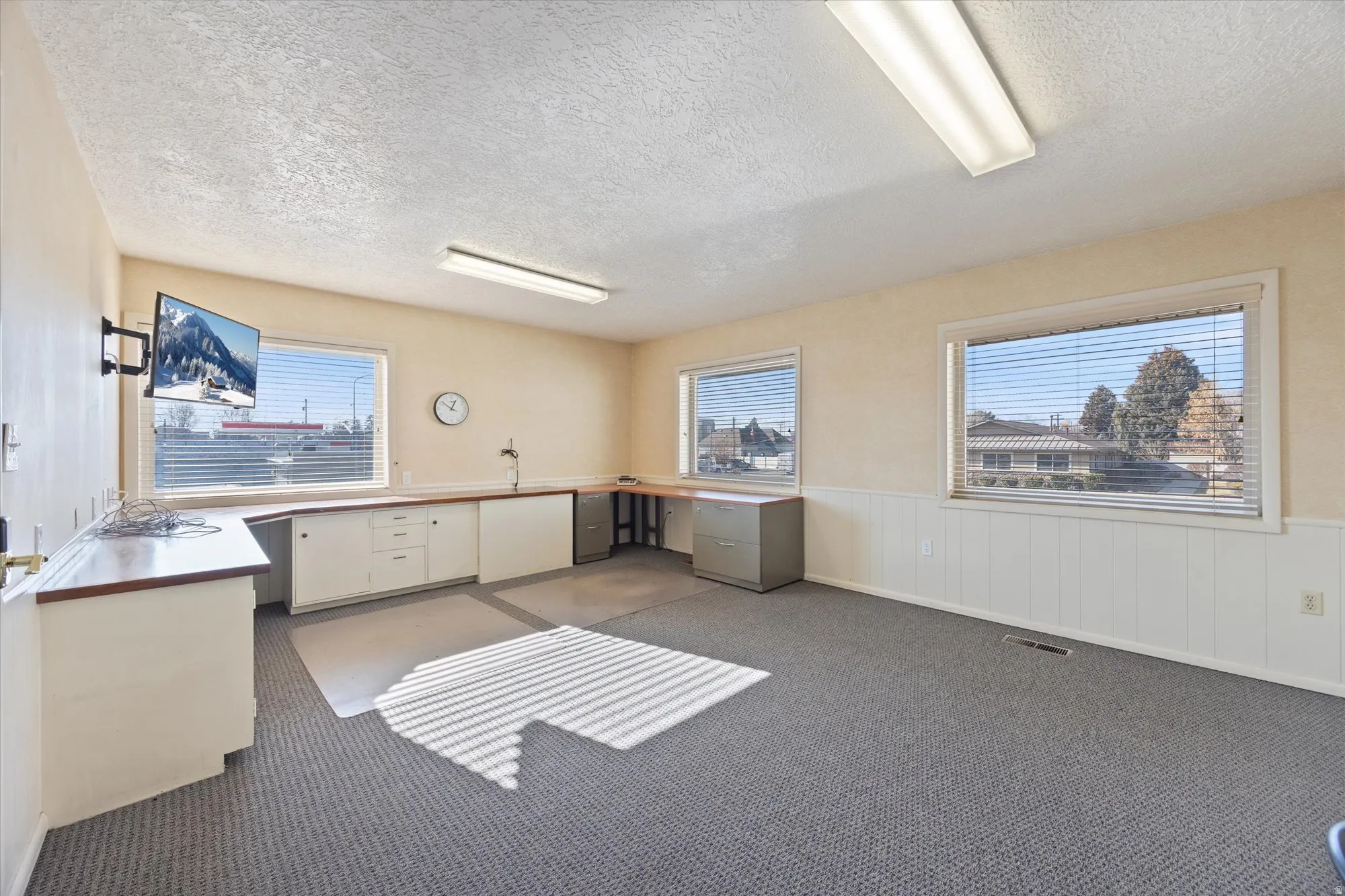 Unfurnished office with a wainscoted wall, a textured ceiling, dark colored carpet, and built in desk