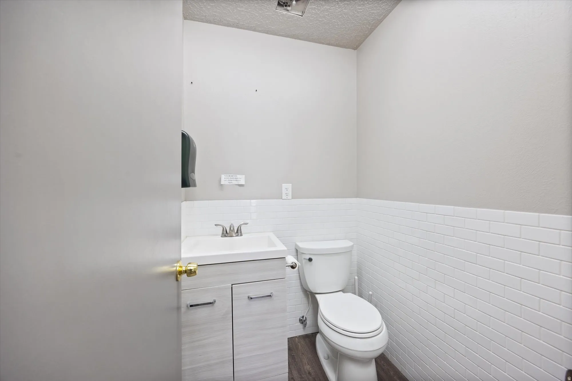 Half bath featuring vanity, a wainscoted wall, a textured ceiling, and tile walls
