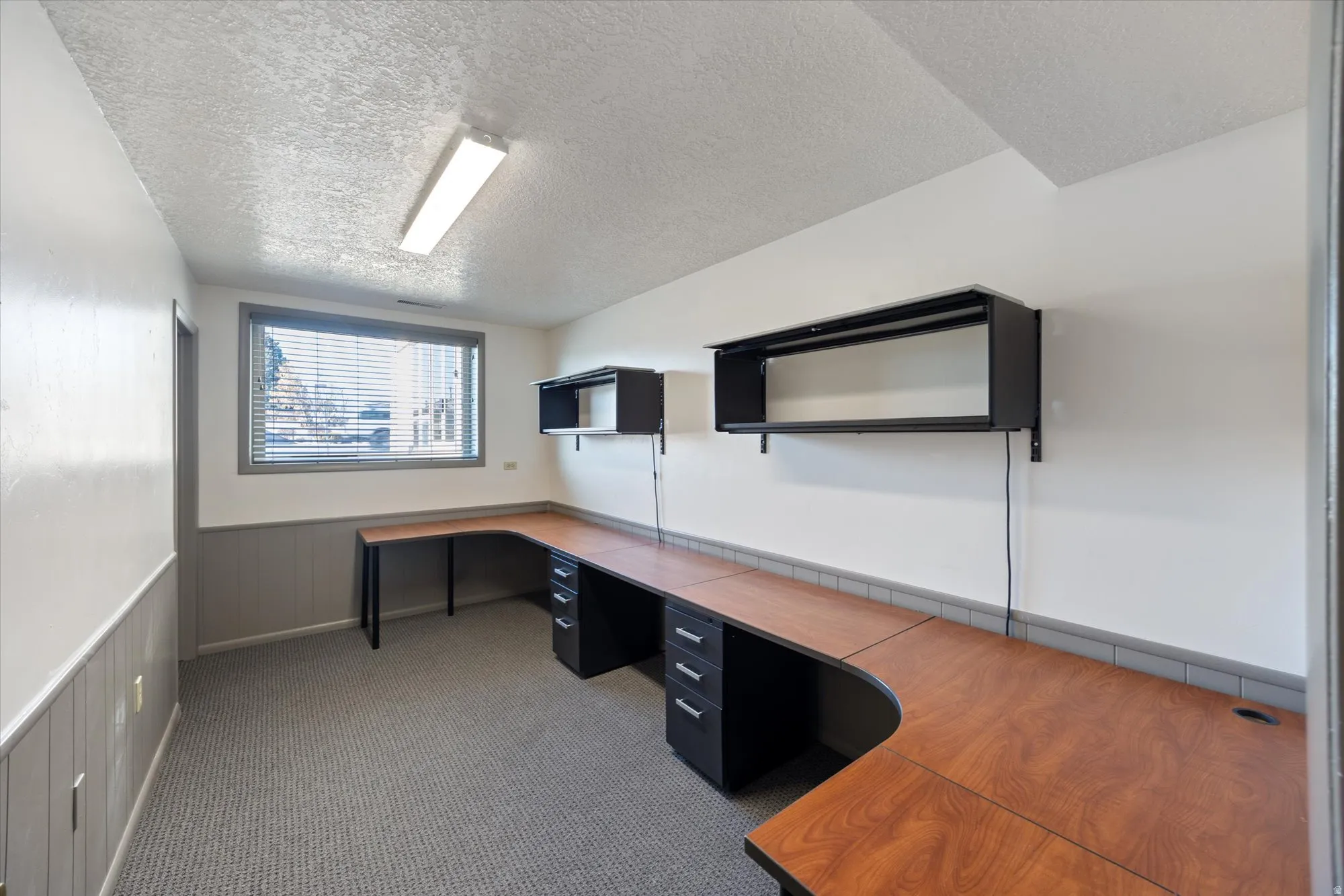 Unfurnished office featuring built in desk, wainscoting, and a textured ceiling