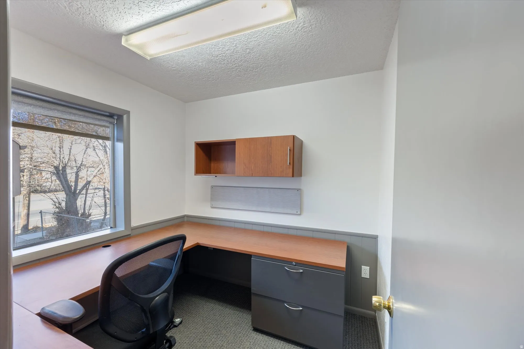 Carpeted home office featuring a textured ceiling and built in desk