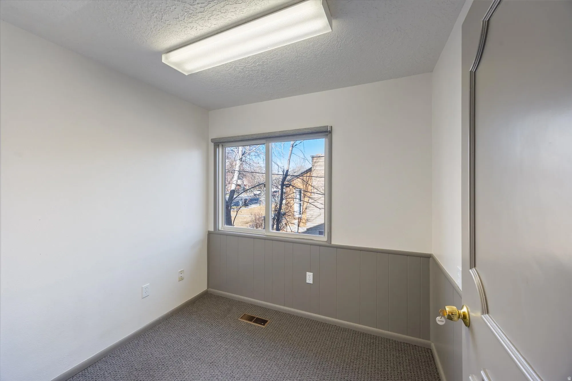 Carpeted empty room with a textured ceiling, a wainscoted wall, and wood walls