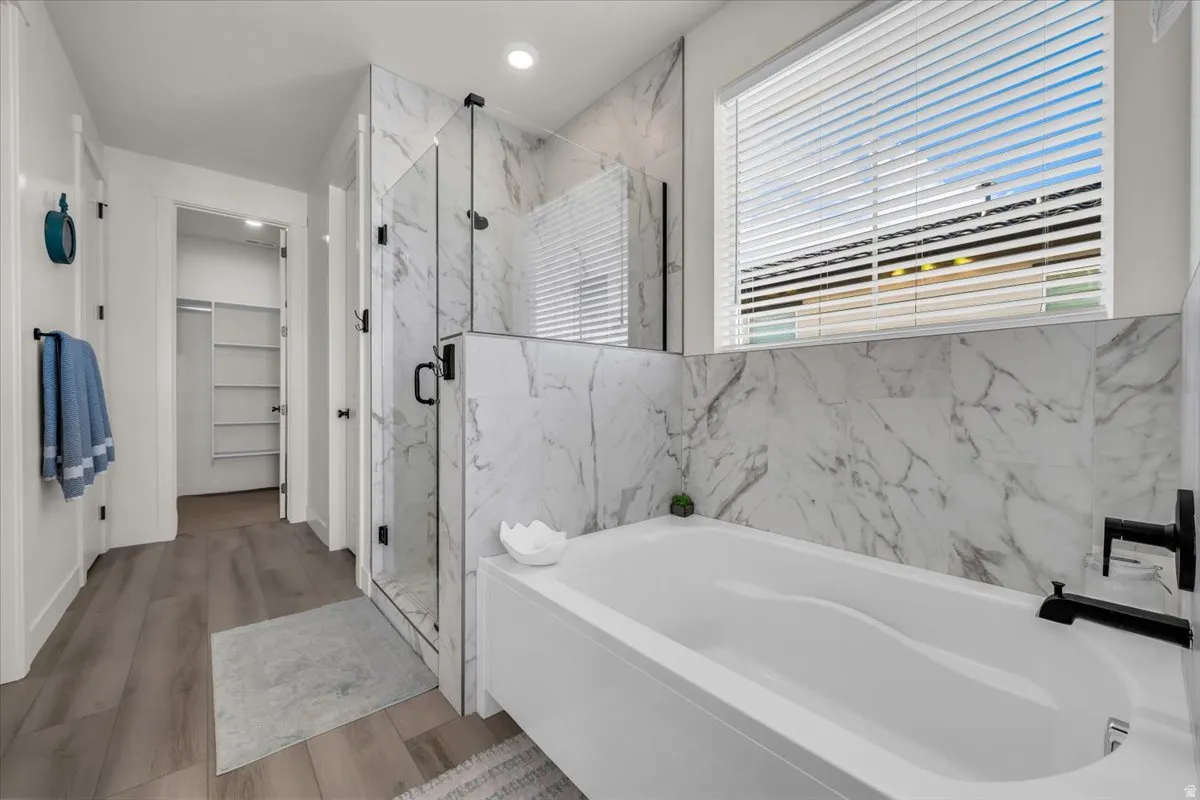 Bathroom with a garden tub, a spacious closet, a marble finish shower, wood finished floors, and recessed lighting