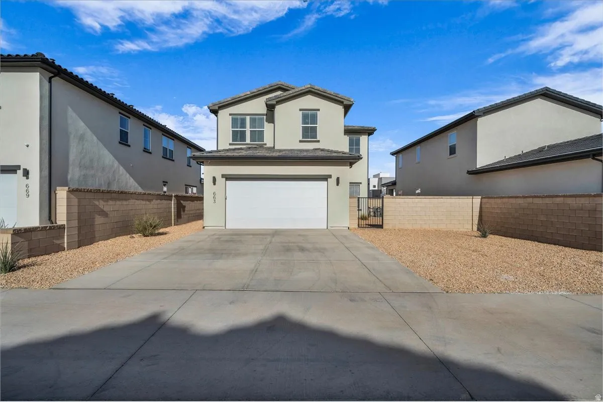 View of front facade with stucco siding, an attached garage, driveway, and a gate