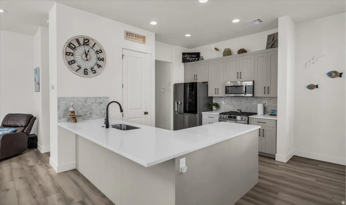 Kitchen with a peninsula, decorative backsplash, stainless steel appliances, dark wood-style flooring, and recessed lighting