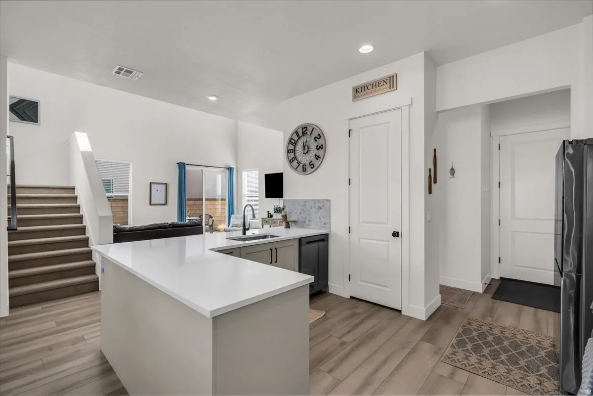 Kitchen with a peninsula, black appliances, light wood-style flooring, recessed lighting, and light stone counters