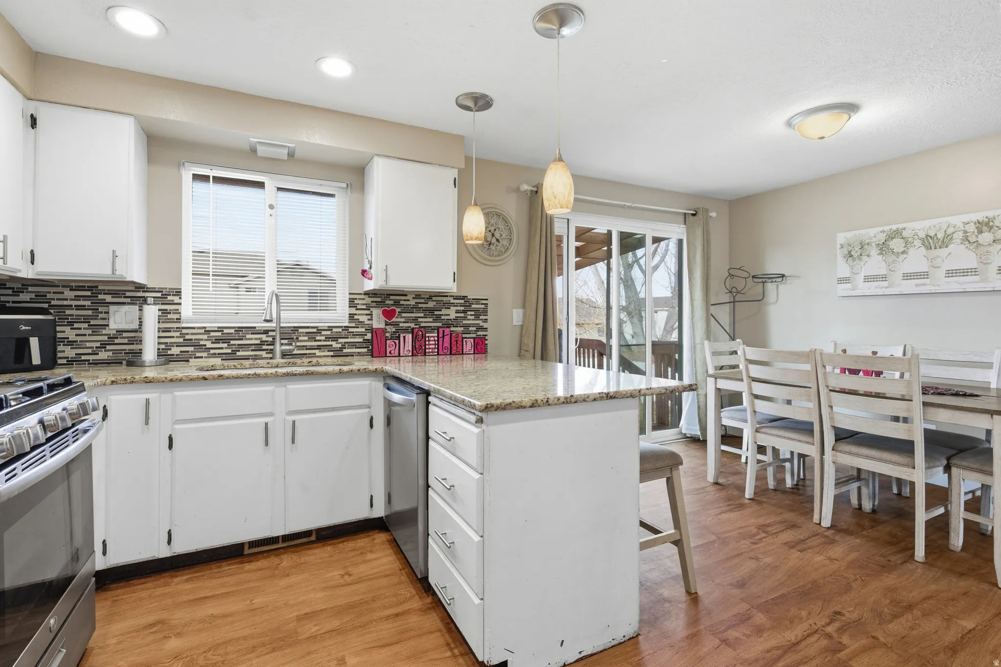 Kitchen with a peninsula, light wood finished floors, decorative light fixtures, and white cabinets