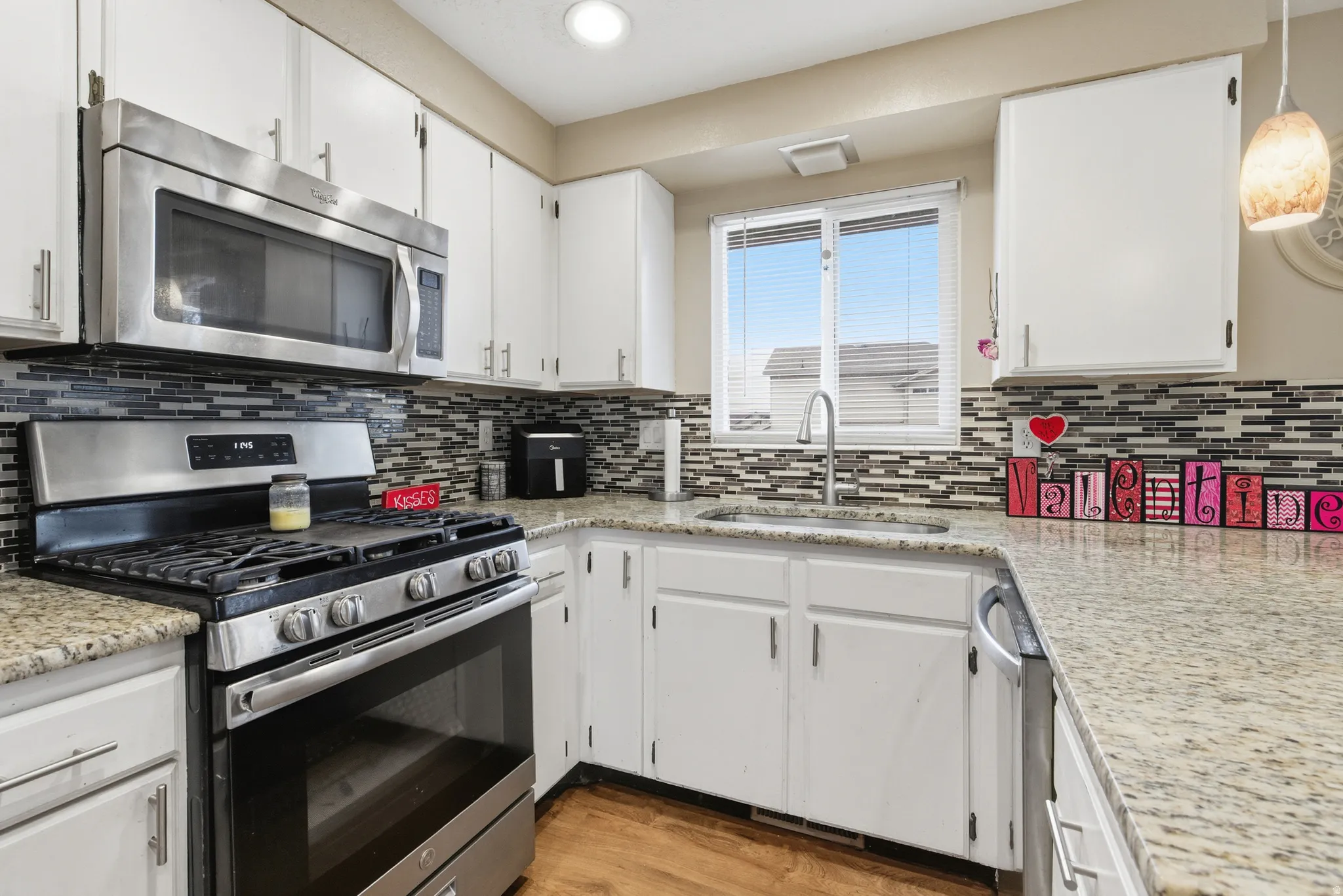 Kitchen featuring stainless steel appliances, white cabinetry, light stone counters, and tasteful backsplash