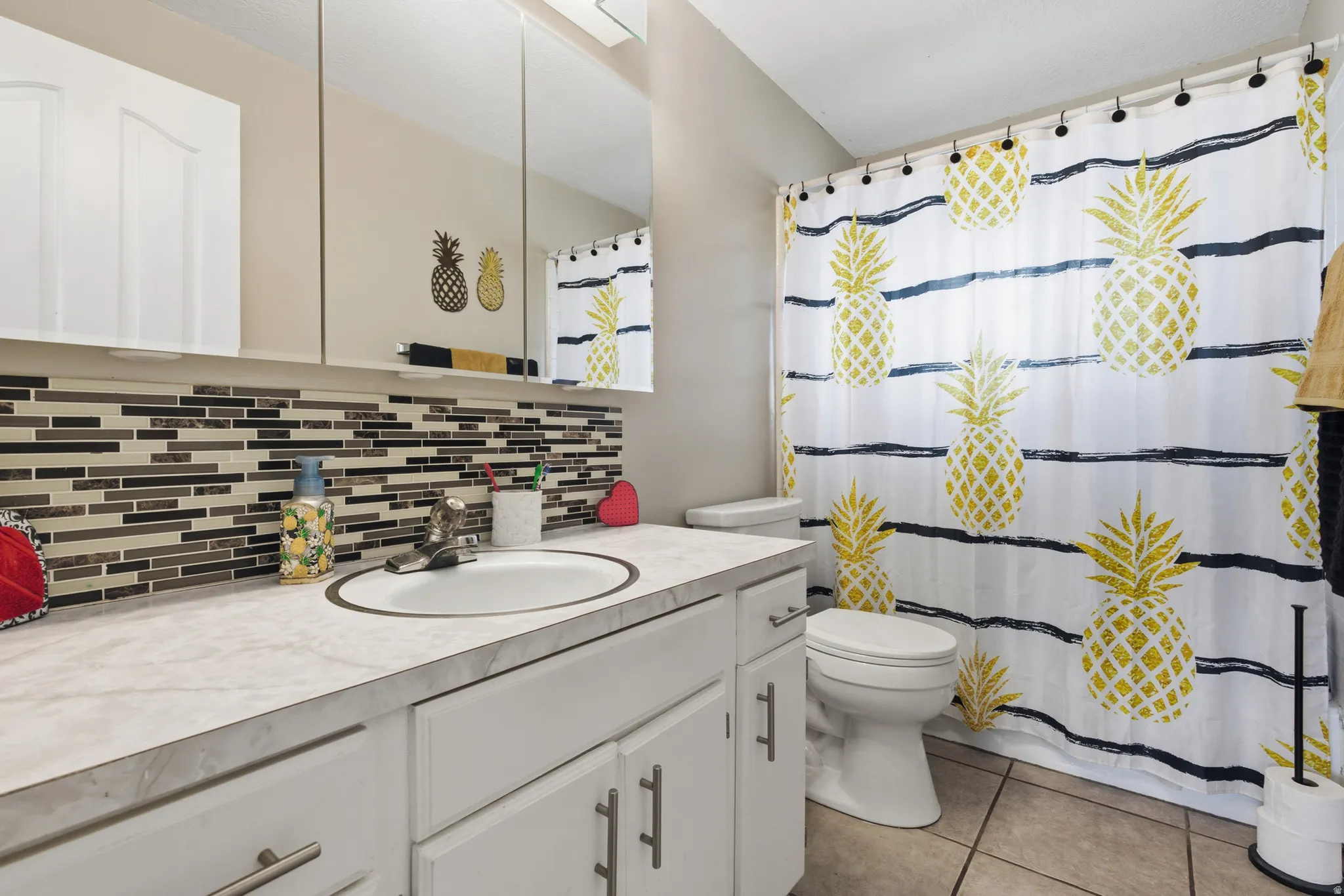 Full bath featuring vanity, a shower with shower curtain, decorative backsplash, and light tile patterned floors
