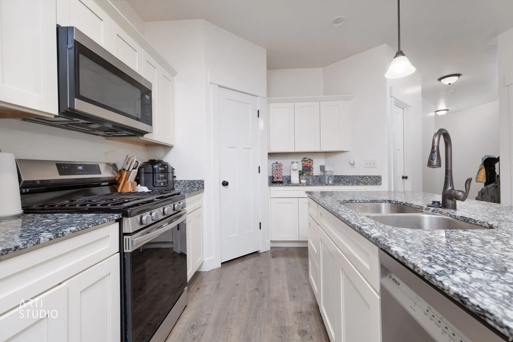 Kitchen with stainless steel appliances, decorative light fixtures, white cabinets, light stone counters, and light wood-style flooring