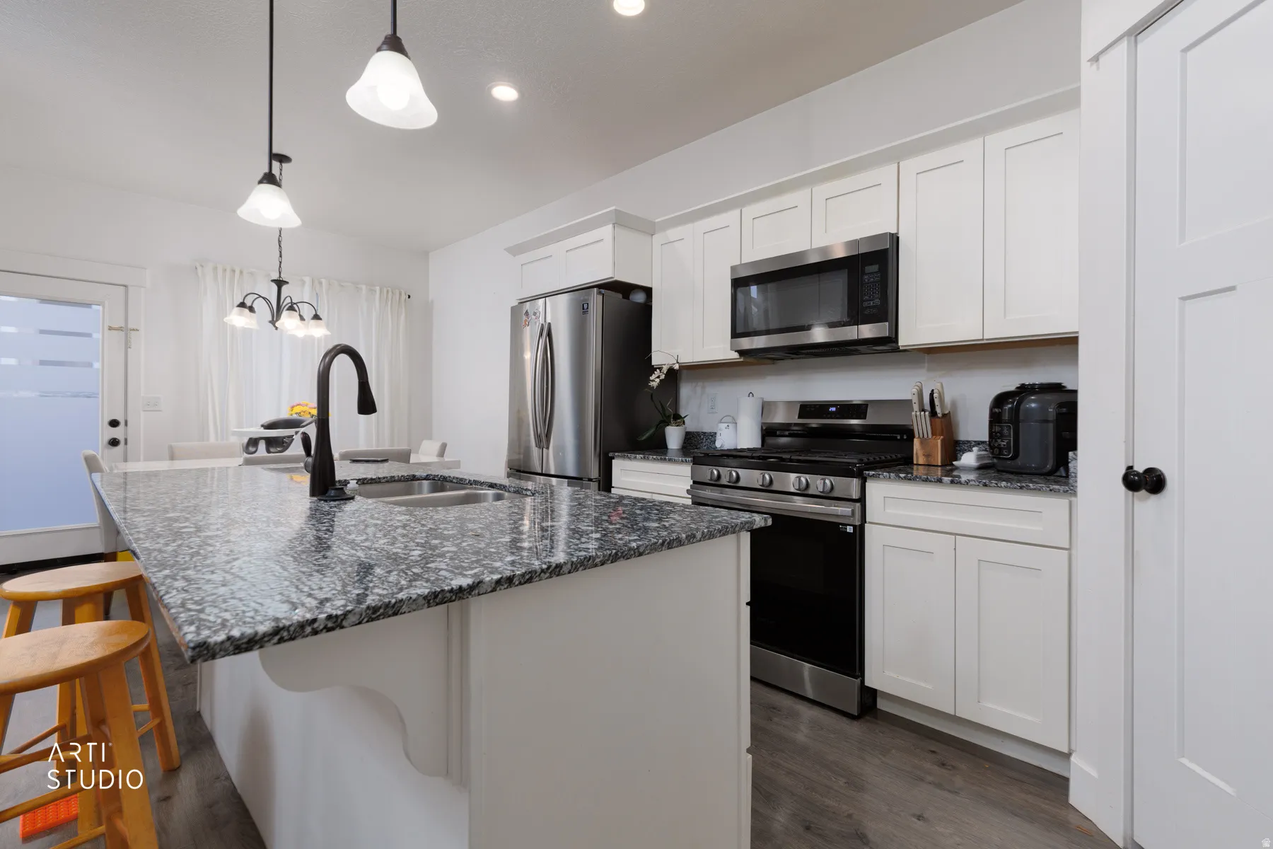 Kitchen with stainless steel appliances, dark stone counters, white cabinetry, a kitchen island with sink, and suspended lighting