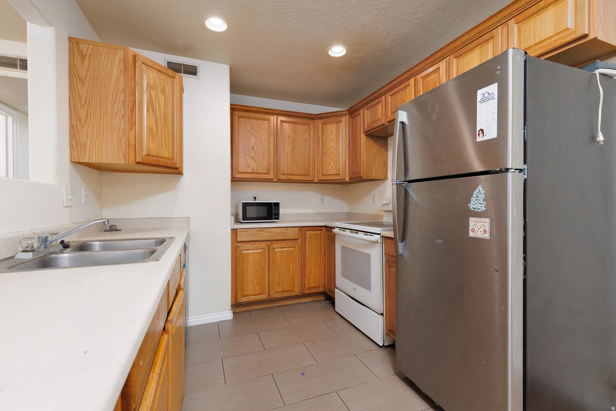 Kitchen featuring freestanding refrigerator, light countertops, white electric range oven, black microwave, and recessed lighting