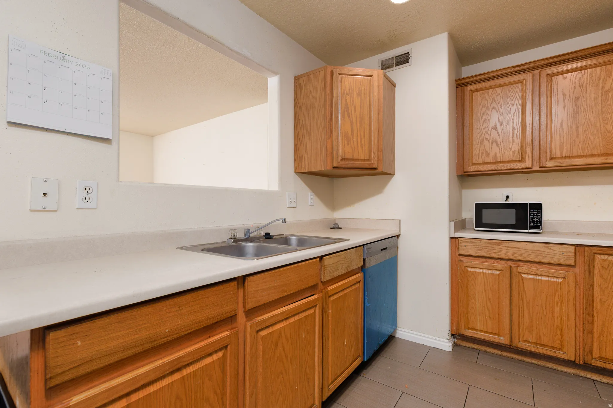 Kitchen featuring light countertops, dishwasher, black microwave, and a textured ceiling