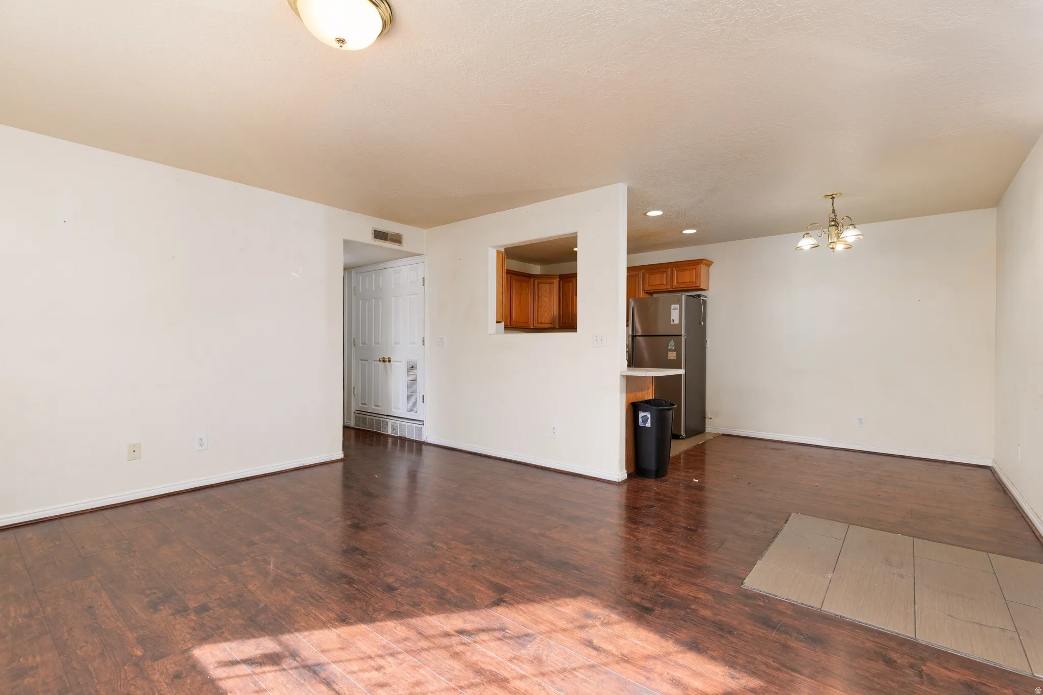 Unfurnished living room featuring a chandelier and dark wood-style floors