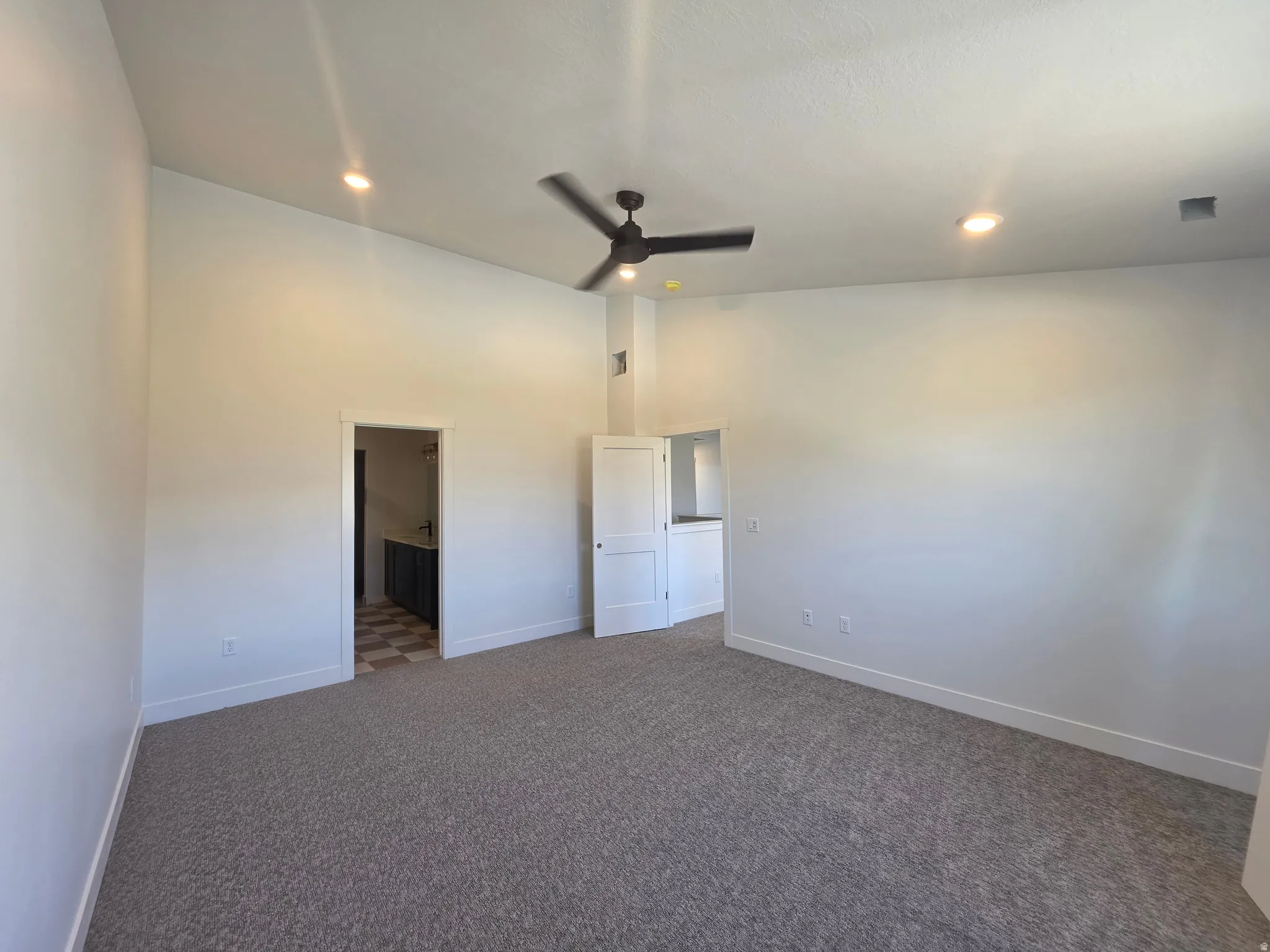 Unfurnished bedroom featuring a ceiling fan, dark carpet, ensuite bathroom, lofted ceiling, and recessed lighting