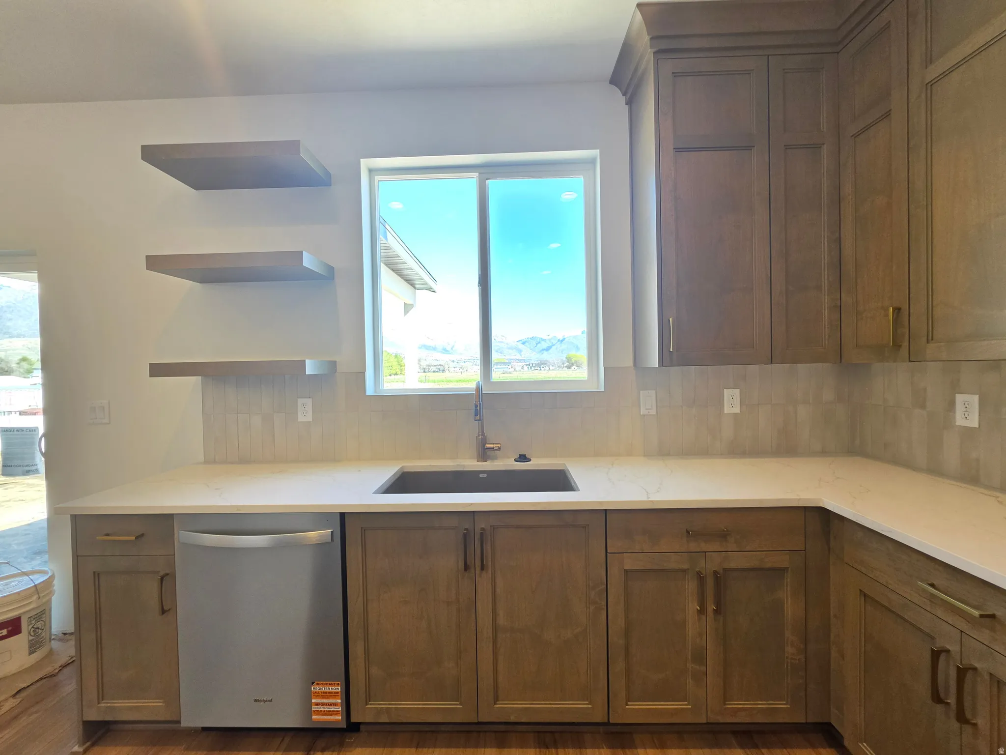 Kitchen featuring tasteful backsplash, open shelves, stainless steel dishwasher, light stone countertops, and dark wood-type flooring