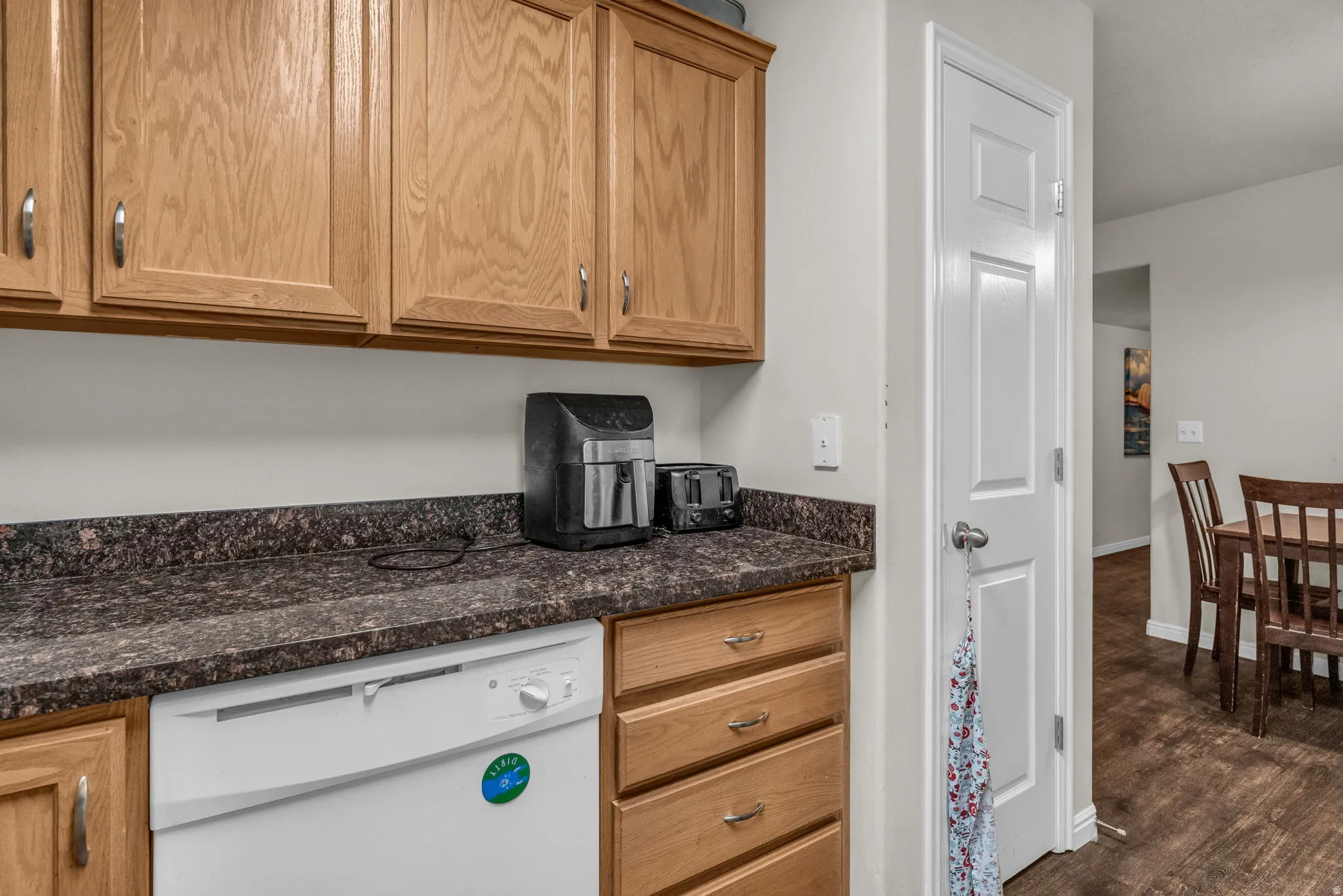 Kitchen featuring dishwasher, wood finish cabinets, dark wood-type flooring, and dark stone counters
