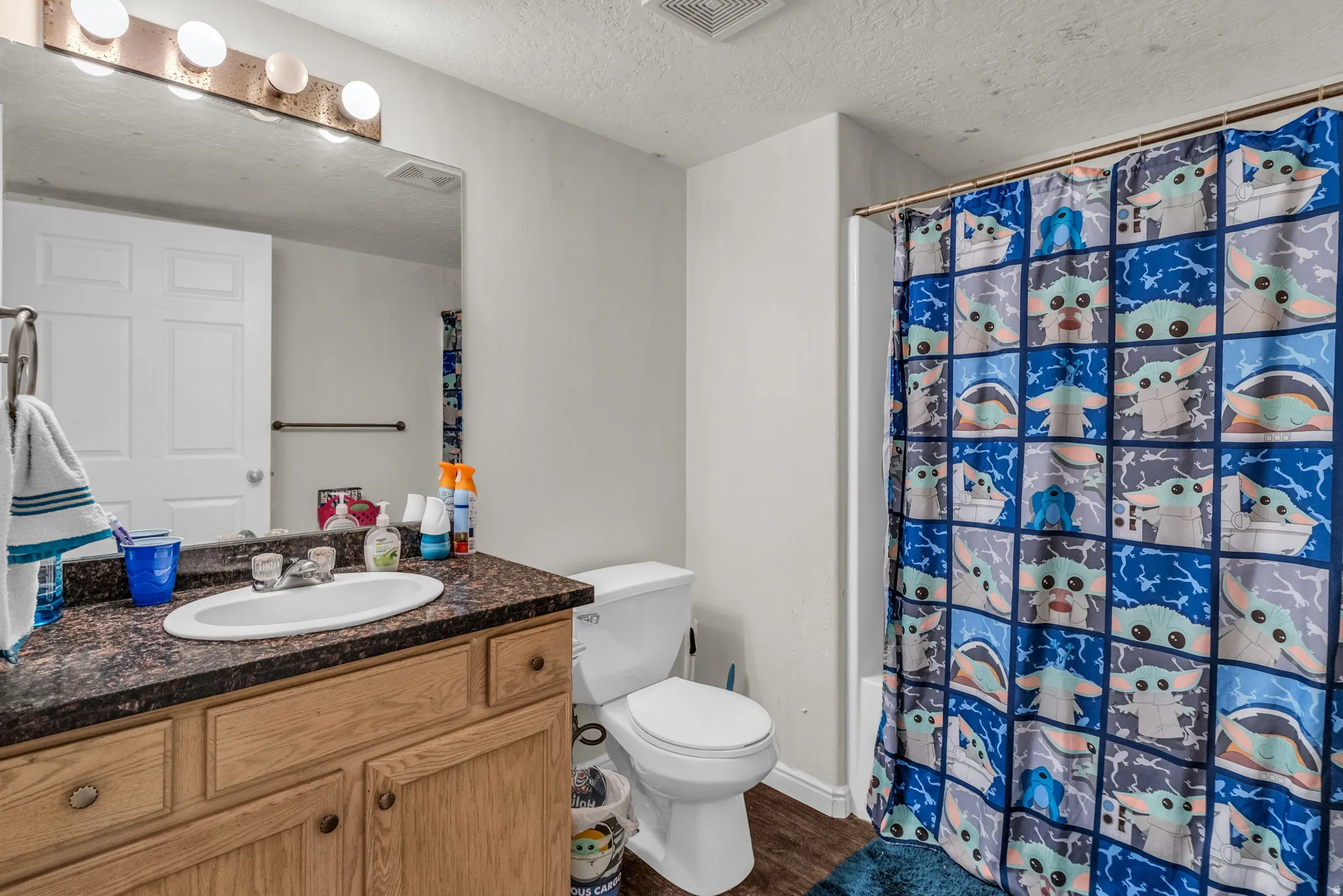 Bathroom with vanity, a textured ceiling, dark wood-style floors, and shower / bath combo
