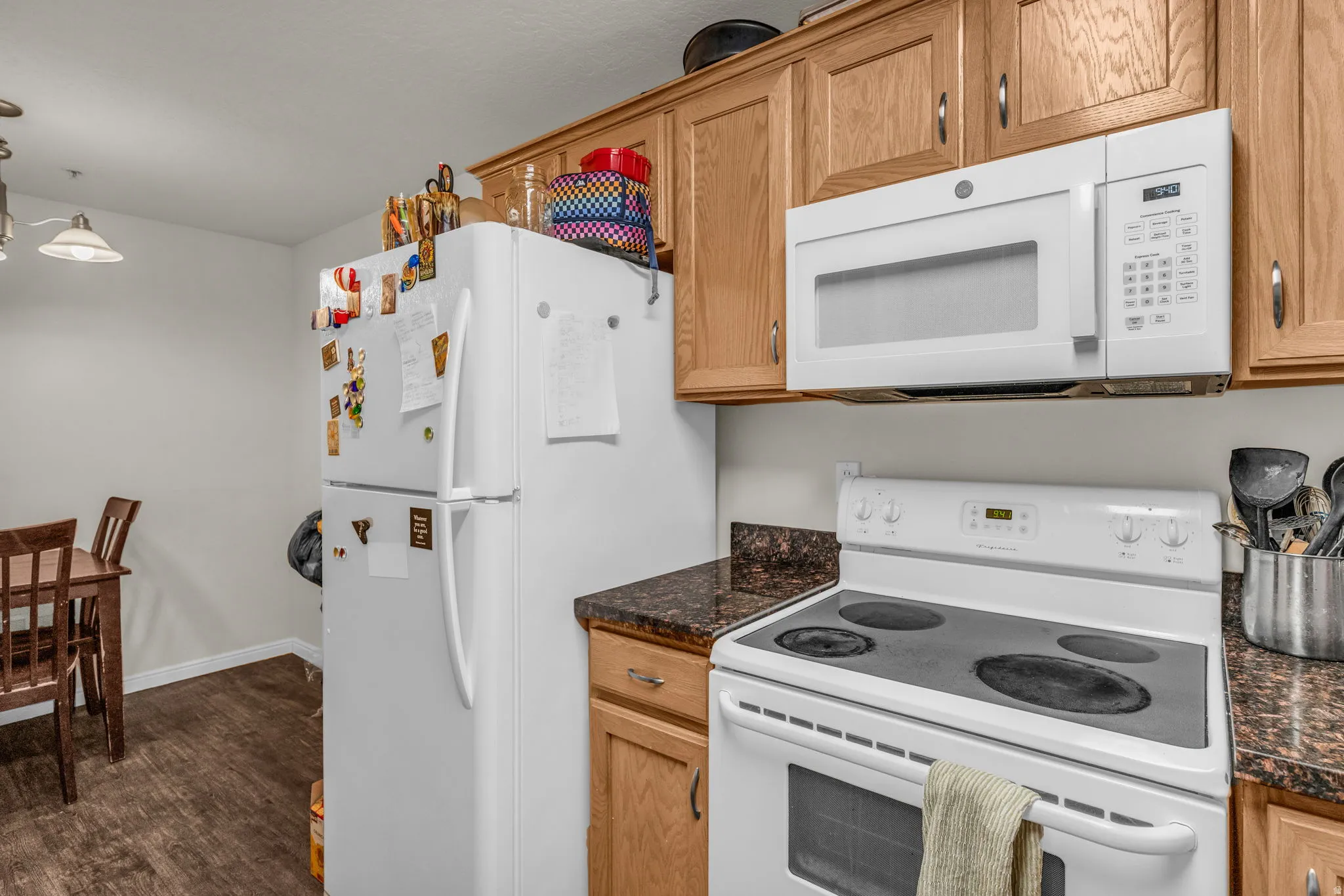 Kitchen with white appliances, pendant lighting, dark wood-style flooring, and dark stone counters