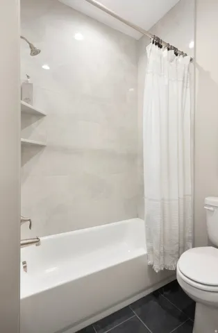 Bathroom featuring shower / bath combination with curtain and dark tile patterned flooring