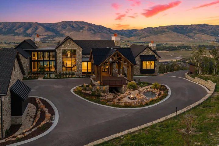 Stone exterior with multiple rooflines, expansive windows, a covered entry, a circular drive, and a retaining wall