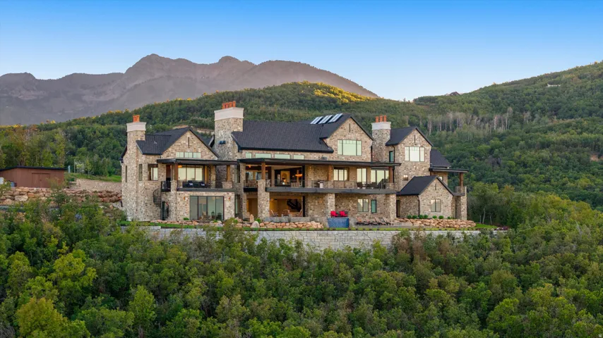 Stone exterior with multiple balconies, expansive windows, dark roof, and a prominent mountain backdrop