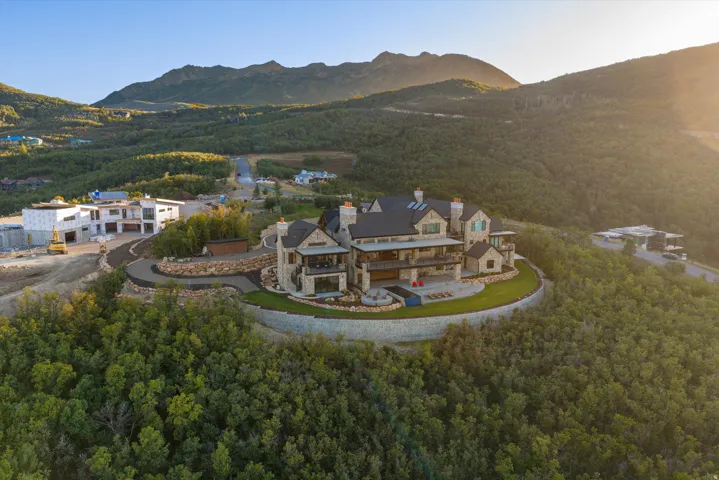 Expansive mountain estate with a stone and wood-clad exterior, multiple balconies, a terraced lawn, and a paved driveway