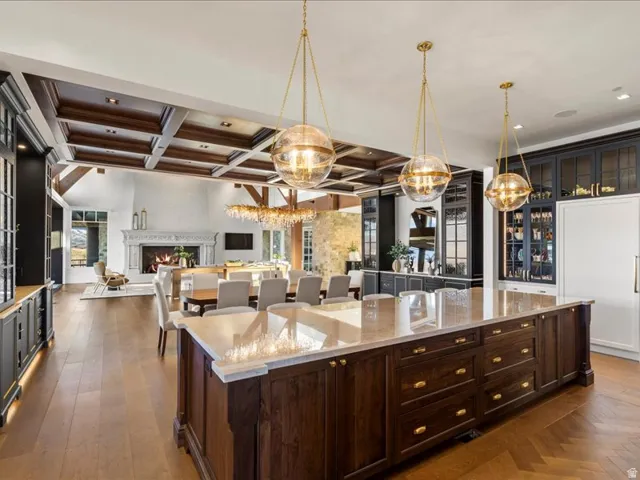 Kitchen featuring coffered ceiling, light stone countertops, hanging light fixtures, dark wood finish cabinetry, and open floor plan