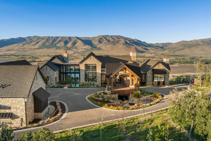 Stone exterior residence featuring multiple gables, extensive window walls, a covered wooden deck, and a circular driveway