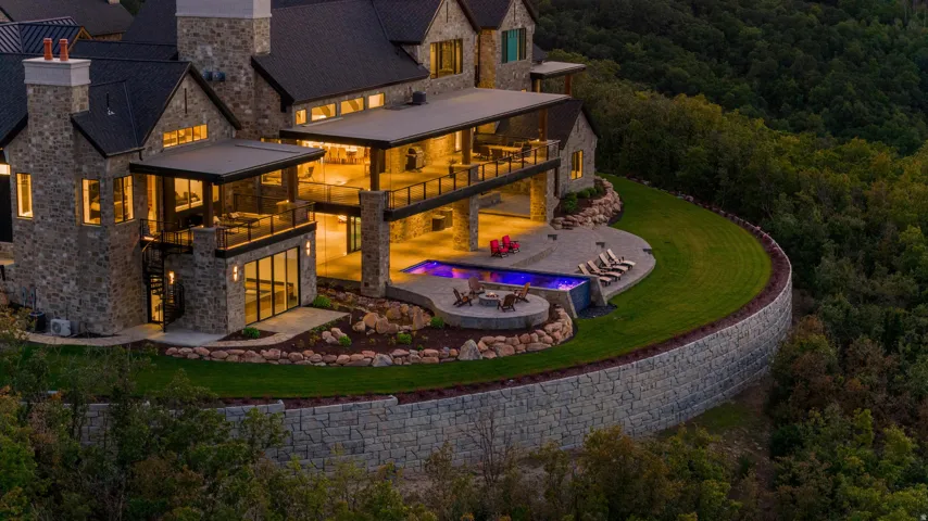 Stone exterior with multiple covered balconies, an infinity-edge pool, a built-in fire pit, and a tiered retaining wall