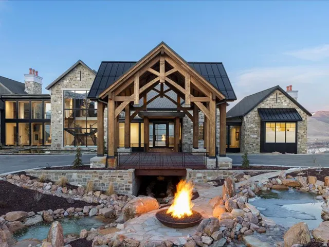 Back of property with a standing seam roof, stone siding, a small pond, an outdoor fire pit, and solar panels