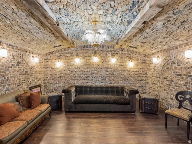 Living area featuring brick wall, dark wood-type flooring, suspended lighting, and beamed ceiling